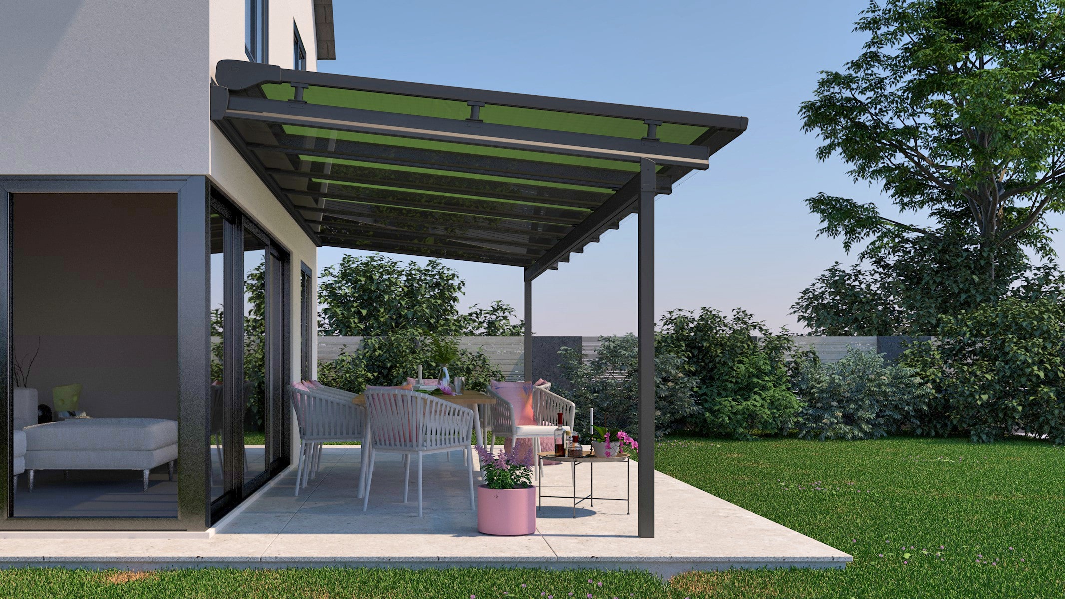 Eine Markise, die an einem hellen Haus befestigt ist und eine Terrasse überdacht. Auf der Terrasse stehen Gartenmöbel und Pflanzenkübel in rosa. Außerdem sieht man grünen Rasen.